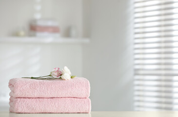 Stack of clean soft towels with eustoma flowers on white table indoors. Space for text