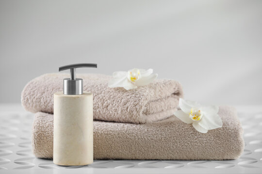 Soft folded towels, orchid flowers and dispenser on white table