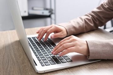 Woman working on laptop at wooden table in office, closeup