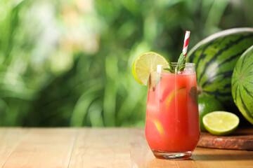 Glass of freshly made watermelon juice with lime and mint on wooden table outdoors, space for text