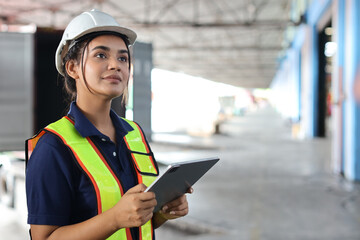 Warehouse workers woman with hardhats and reflective jackets using tablet, walkie talkie radio...