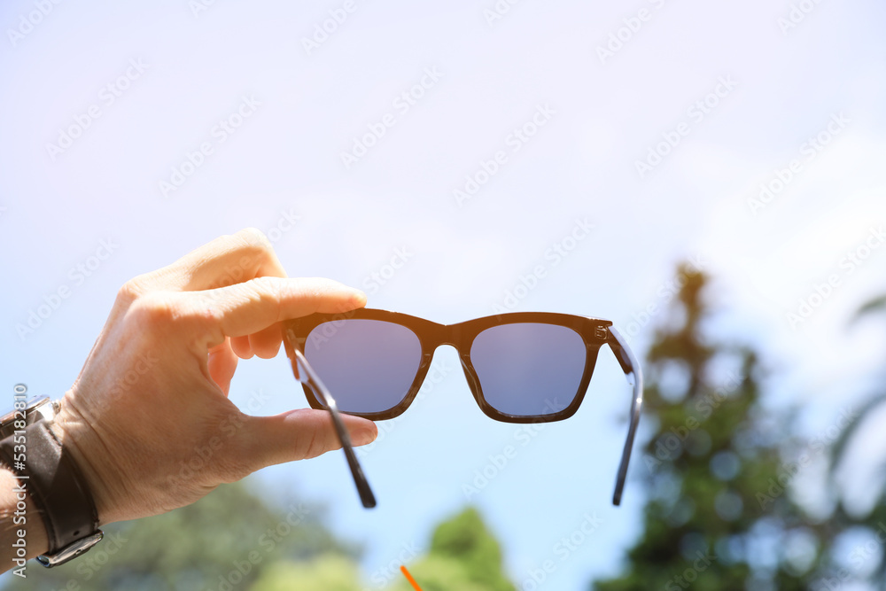 Sticker mature man holding stylish sunglasses outdoors on sunny day, closeup