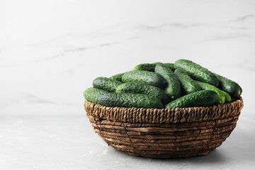 Fresh ripe cucumbers in wicker basket on marble table, space for text