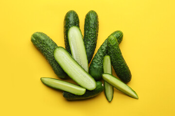 Whole and cut fresh cucumbers on yellow background, flat lay