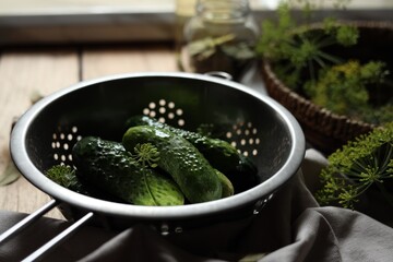 Fresh cucumbers in colander and other ingredients prepared for canning on wooden table, closeup