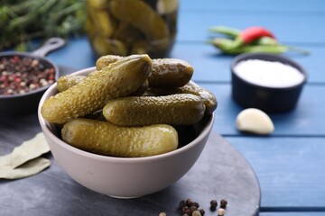 Bowl of pickled cucumbers and ingredients for food preservation on blue wooden table, closeup