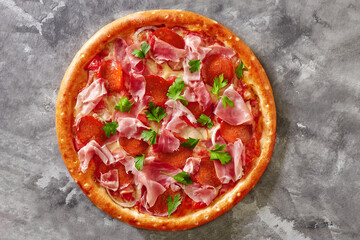 Meat pizza with salami, smoked chicken, ham and prosciutto on gray stone surface
