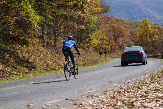 Ciclista solo circulando detrás de un coche en una carretera en otoño
