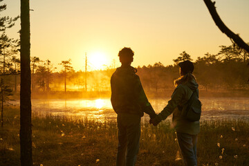 woman and man holds hands tourist meets dawn in nature. Sunset,  light and fog, Reflections of trees in lakes . Travel romance. Viru swamps Estonia.