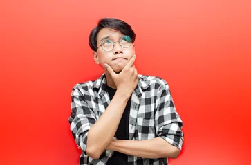 Fotobehang Thoughtful asian man thinking and wondering with hand touching skin as thinking gesture isolated over red background. © Teo
