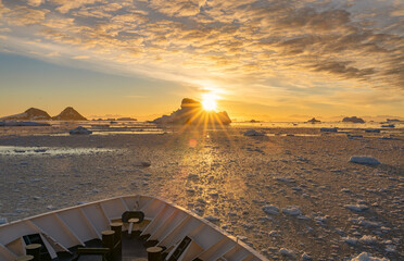 Kreuzfahrtschiff fährt bei einen dramatischer Sonneuntergang / Abendstimmung durch die winterliche Cierva Cove - ein tiefer Meeresarm an der Westseite der Antarktischen Halbinsel, umringt von der Cier - obrazy, fototapety, plakaty