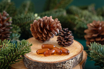  Oil capsules near fir branches and pine cones close up. Taking dietary supplements