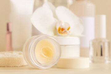 Fototapeta na wymiar Smass Glass jar and other cosmetics near white orchid flower on beige close up