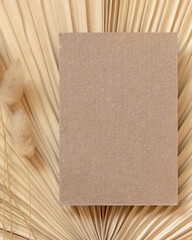 Blank card on dry beige palm leaf near hare's tail grass top view,  boho wedding mockup