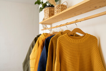 Autumn knitted sweaters hang on wooden hangers in the room