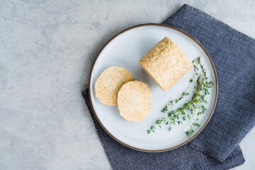 Top view raw Tempeh or Tempeh, made of fermented soybean seeds. Tempeh Slices on plate with herbs. Soya protein. Plant based meat concept. Healthy Cooking and eating. Go vegan. Flat Lay, copy space