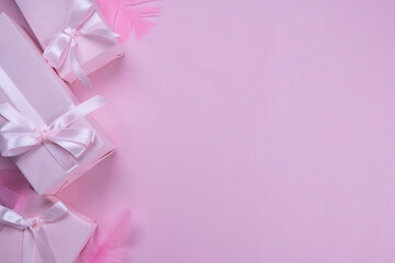 background with pink gift boxes with pink bows on a pink background with a place to insert text, copy space, decorated with feathers, top view, the concept of celebrating a girl's birthday, party