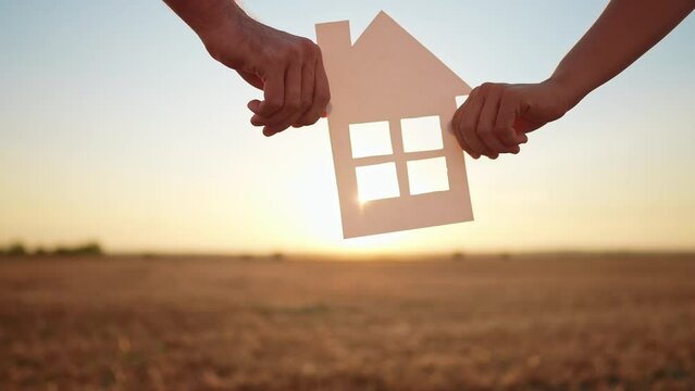 paper house happy family. friendly family hands holding paper house the glare of the sun shine through the window a beautiful sunset lifestyle. mortgage business construction concept. house dreams