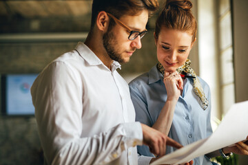 Portrait of two young business people talking about documents in office