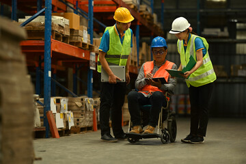 Male manager in wheelchair and workers working together in warehouse. Manufacture storehouse...