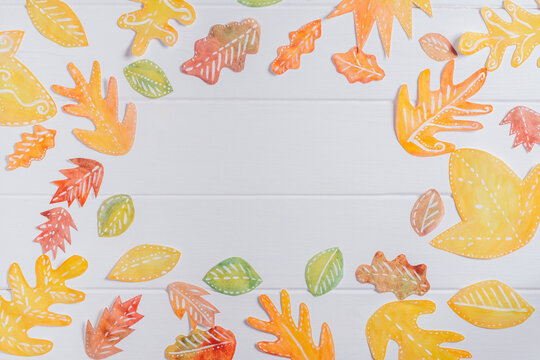 Background image of cut paper red, orange and yellow autumn leaves painted in watercolor laid out on white wooden planks. top view. Copy space. DIY handmade autumn decorations