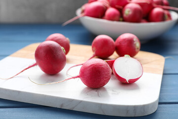 Board with fresh ripe radishes on blue wooden table, closeup