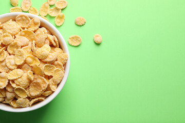 Bowl of tasty crispy corn flakes on light green background, flat lay. Space for text