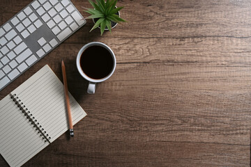 Simple workplace with notepad, coffee cup and wireless keyboard on wooden table. Top view with copy...
