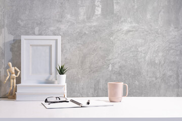 Blank picture frame, books, coffee cup and small potted plant on white table. Copy space for text.