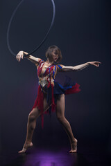 Beautiful woman performing acrobatic element on aerial ring indoors. Circus performer doing trick on arial lira on black background.