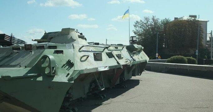 broken green infantry fighting vehicle. Flag of Ukraine flutters in the wind. War, an exhibition of military equipment in the open air.