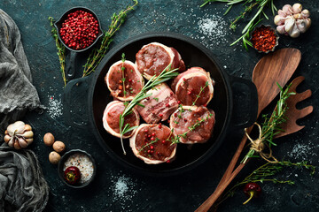 Meat. Raw Meat Veal medallions wrapped in bacon. Laid out in a pan, ready to cook. On a black...