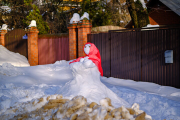 A snowman in a red shawl. Suburban Winter landscape. Selective focus.