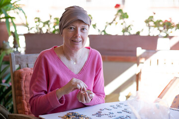 Woman undergoing chemotherapy treatment for breast cancer assembles a puzzle on the terrace of her house