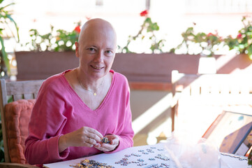 Woman undergoing chemotherapy treatment for breast cancer assembles a puzzle on the terrace of her...