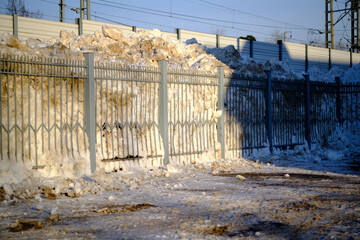 Huge snowdrifts behind a metal fence. Suburban Winter landscape. Selective focus.