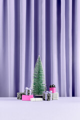 Minimal christmas present concept with hot pink gifts with bows under the pine tree on purple violet curtain background. Giving season, New Year, festive, winter aesthetic.
