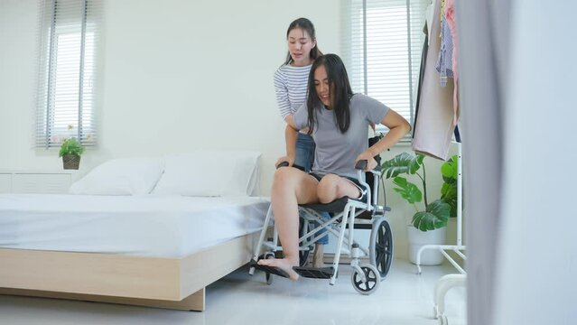 Asian young woman support female leg amputee friend sit on wheelchair.