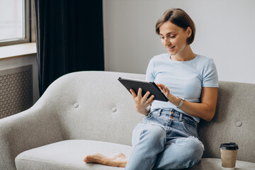 Woman sitting home on a sofa and reading book on a tablet