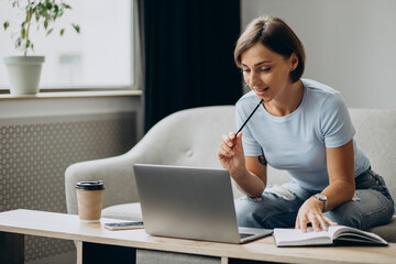 Woman studying at home online on laptop and making notesa