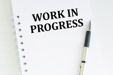 text WORK IN PROGRESS on a notepad on the table, a business concept.