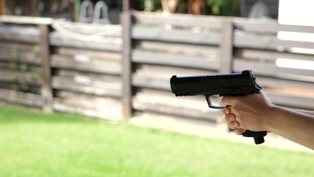 Young woman's hand holding, aiming and shooting a black metal bb gun or pistol. Close up shot, unrecognizable people, slow motion