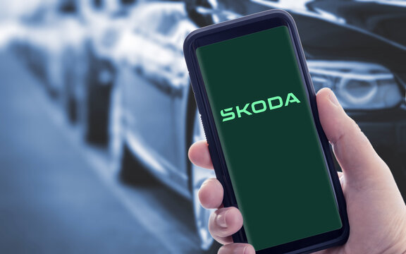 Galicia, Spain; january 09 2021: Hand holding a smart phone with new SKODA logo on screen. Blurry cars at background