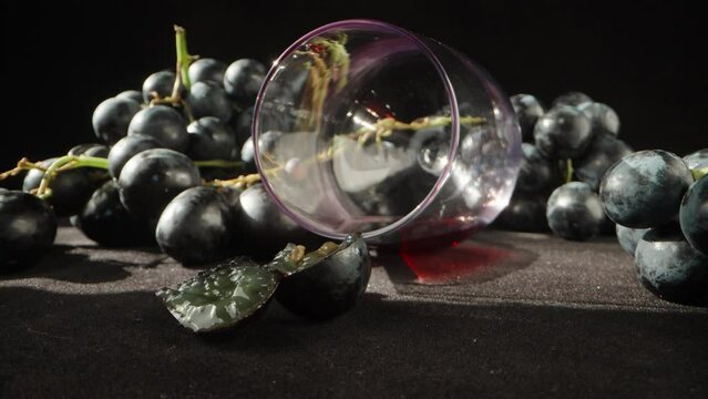 A glass of wine overturned on a black table and black grapes. panorama, close-up.