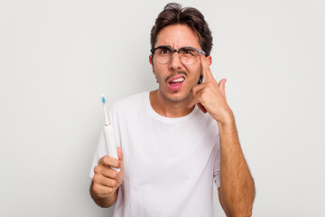 Young hispanic man holding electric toothbrush isolated on white background showing a disappointment gesture with forefinger.