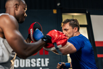 Caucasian man wear boxing gloves punching ahead with African trainer. 