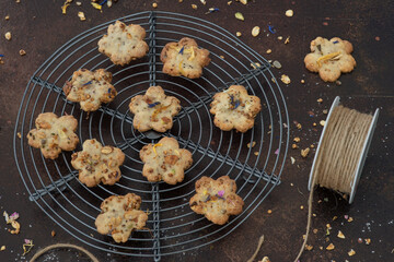 flower shaped cookies with cereal and dried edible flowers, dark background, close up, cookies on a cake rack, rustic