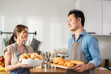 Asian young female holding bread and giving to male in kitchen room. 