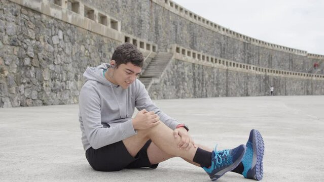 Hispanic teenager boy suffering knee pain. Injured athlete sitting on floor