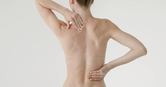 Young woman touches and massages her back. Back problems. Back pain. Girl on a white isolated background